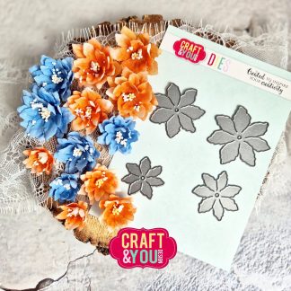 Blue and orange paper flowers arranged beside a sheet of metal flower dies on a lace-covered wooden surface.